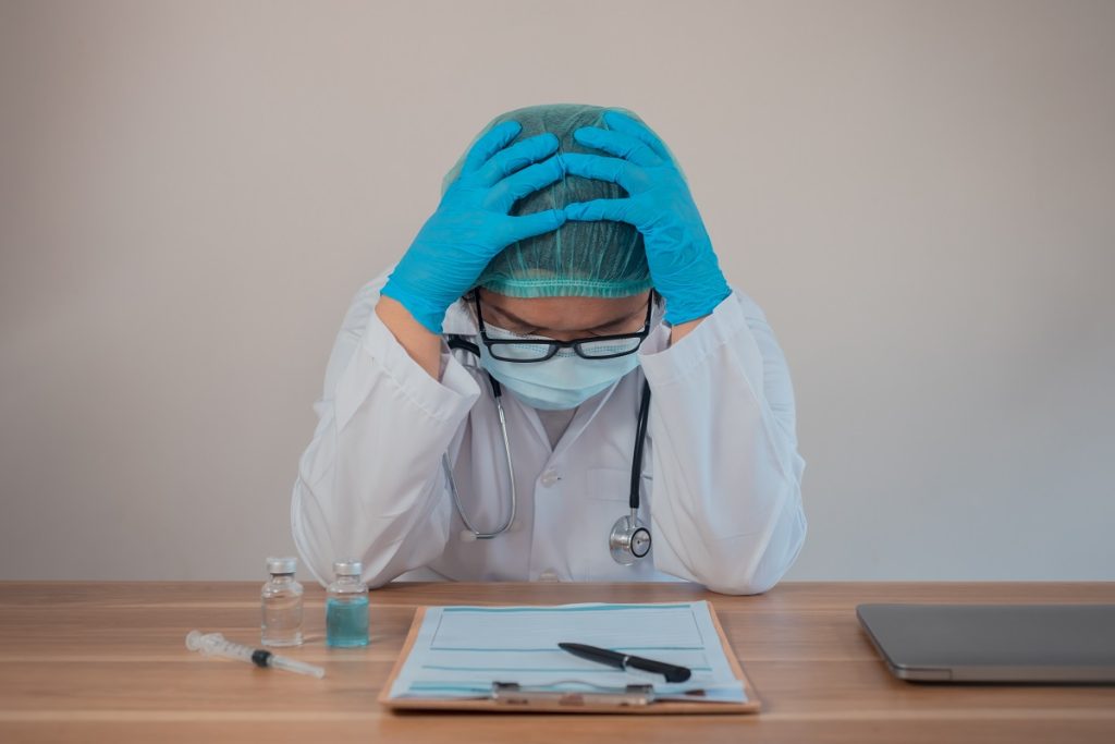 Frustrated doctor with head in hands at desk, illustrating the emotional toll of medical malpractice or wrongful treatment.