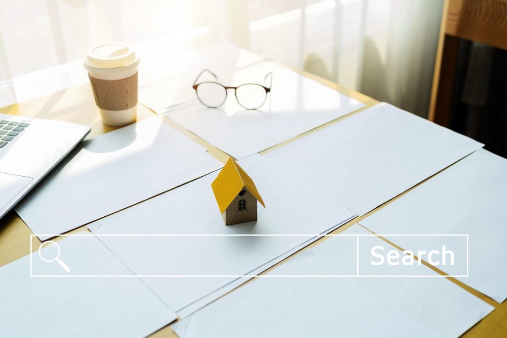 Airbnb için uygun ev arayışı ve yatırım araştırması sürecini gösteren masa üzerindeki belgeler, kahve ve küçük ev maketi.