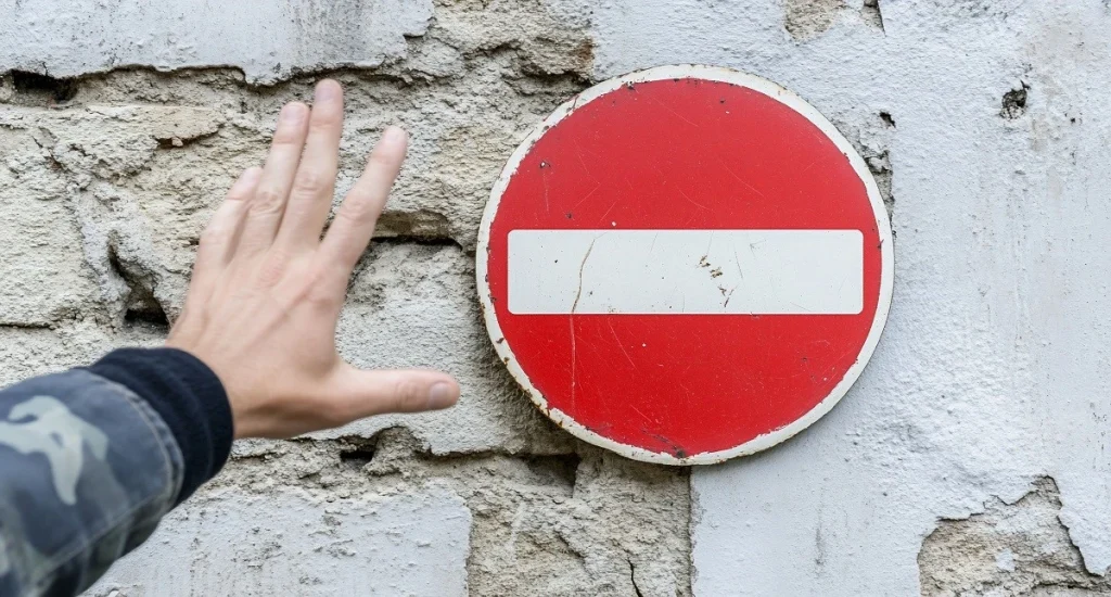 A hand raised toward a no-entry traffic sign on a stone wall — symbolizing restricted entry to Turkey due to a visa ban or overstay penalty.