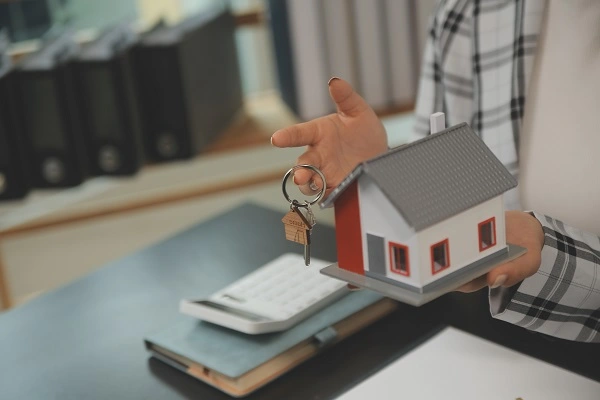 A person handing over a house model and keys symbolizing real estate transfer, illustrating the process of inheriting property in Turkey.